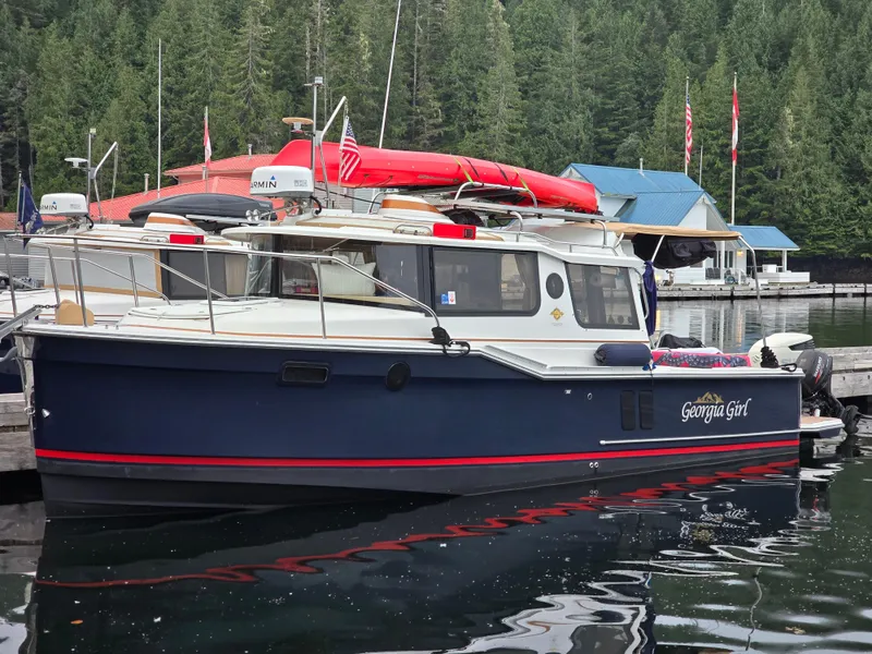 Slide: The Image of 2018 Ranger Tugs R27 OB boat docked, surrounded by forested landscape and marina. - 1