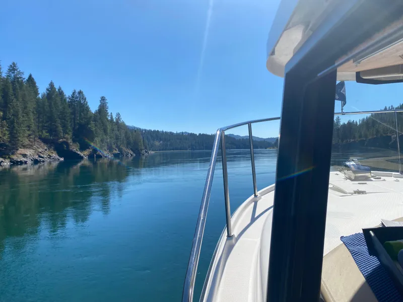 Slide: The Image of 2018 Ranger Tugs R27 OB cruising on a serene lake with forested shoreline. - 2