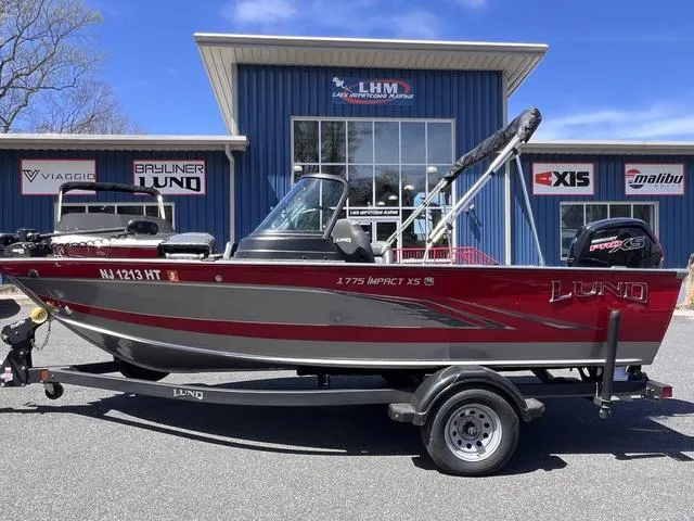 Slide: The Image of 2023 Lund 1775 Impact XS Sport boat on trailer, parked outside dealership. - 1