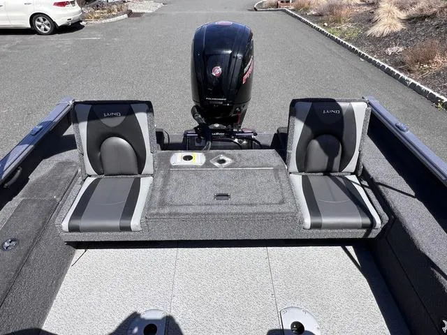 Slide: The Image of 2023 Lund 1775 Impact XS Sport boat interior with seating and motor, parked on pavement. - 16