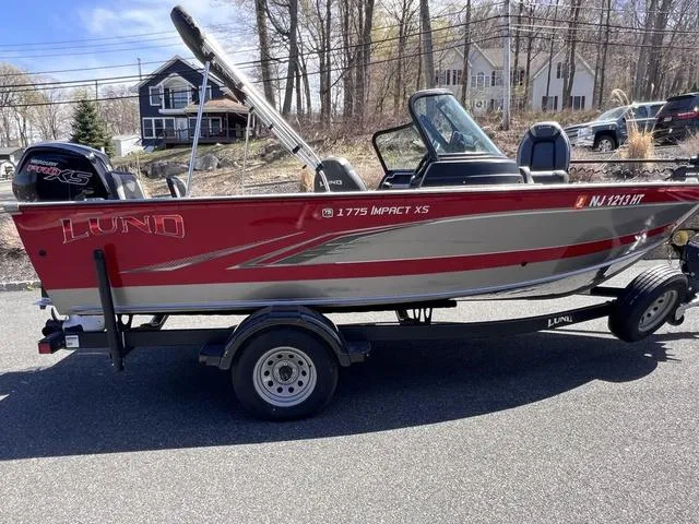 Slide: The Image of 2023 Lund 1775 Impact XS Sport boat on trailer, red and silver design, parked outdoors. - 7