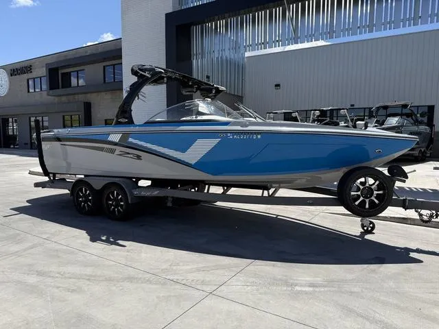 Slide: The Image of 2015 Tigé Z3 boat on trailer, blue and gray, parked outside a modern building. - 2