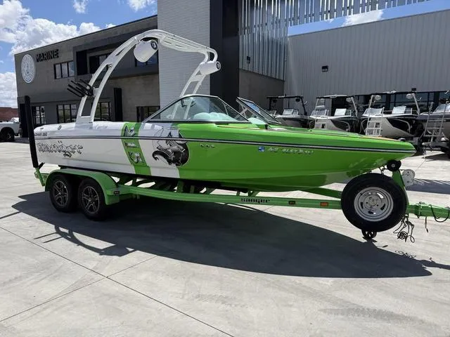 Slide: The Image of 2016 Sanger 215S boat in green and white on a trailer, parked outside a marine facility. - 2