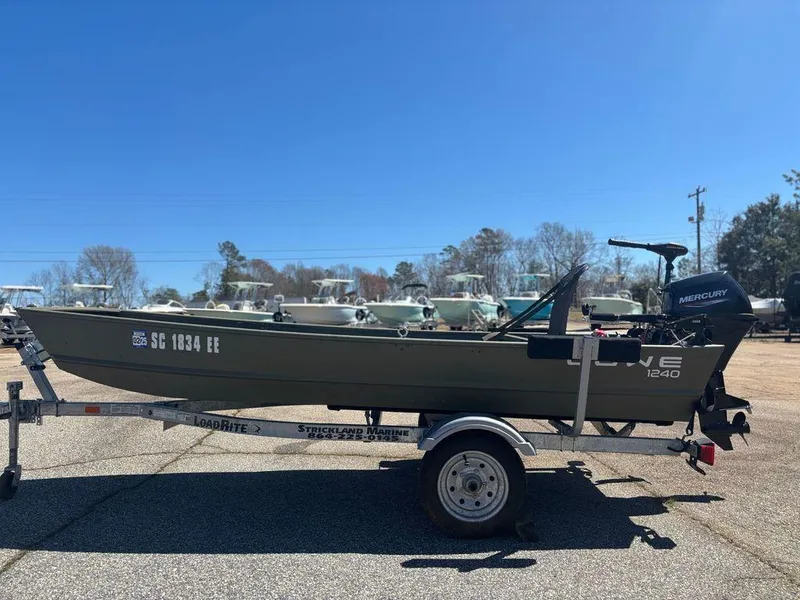 Slide: The Image of 2024 Lowe L1240 Jon boat on trailer, parked outdoors under clear blue sky. - 1