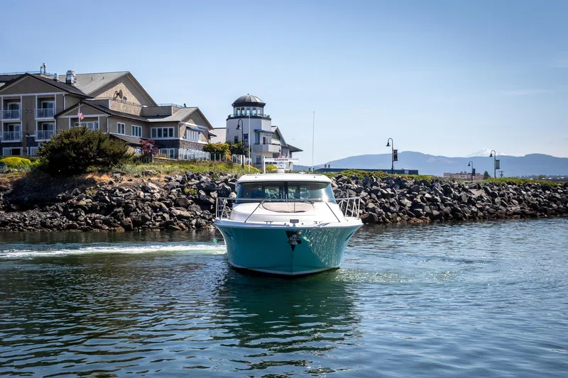 Slide: The Image of 2023 Tiara Yachts C44 Coupe cruising near coastal buildings and rocky shoreline. - 3