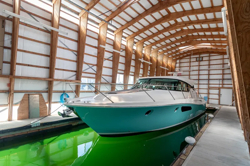 Slide: The Image of 2023 Tiara Yachts C44 Coupe in a covered dock, showcasing sleek design and vibrant hull. - 4