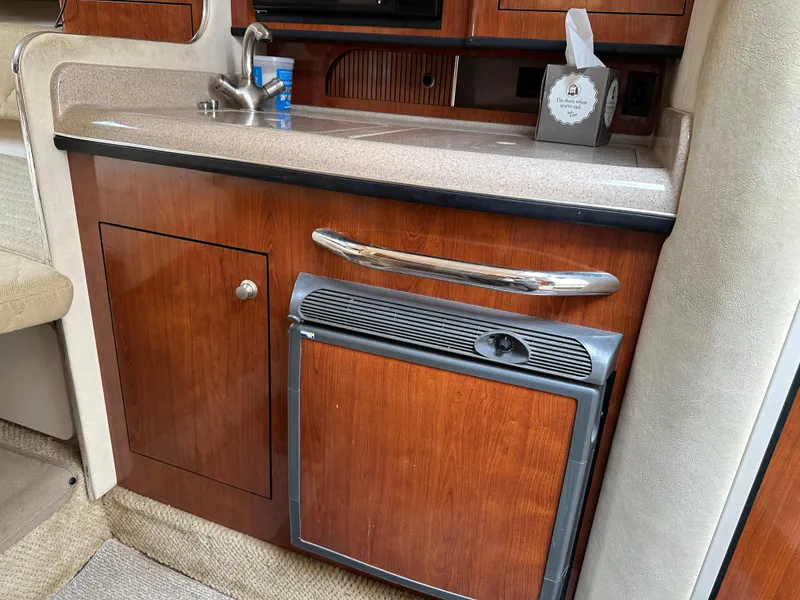 Slide: The Image of Interior of 2006 Sea Ray 280 Sundancer with kitchenette, featuring wood cabinetry and compact fridge. - 14