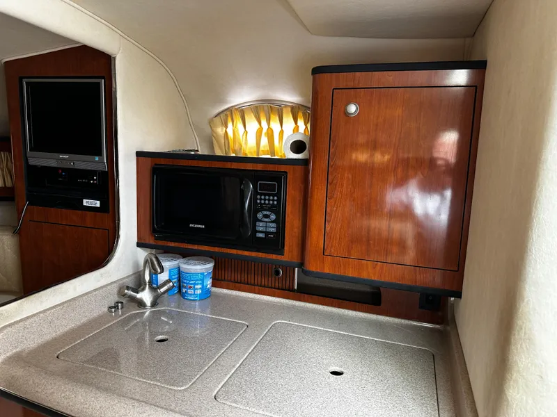 Slide: The Image of 2006 Sea Ray 280 Sundancer interior with kitchenette, featuring microwave, sink, and wooden cabinetry. - 15