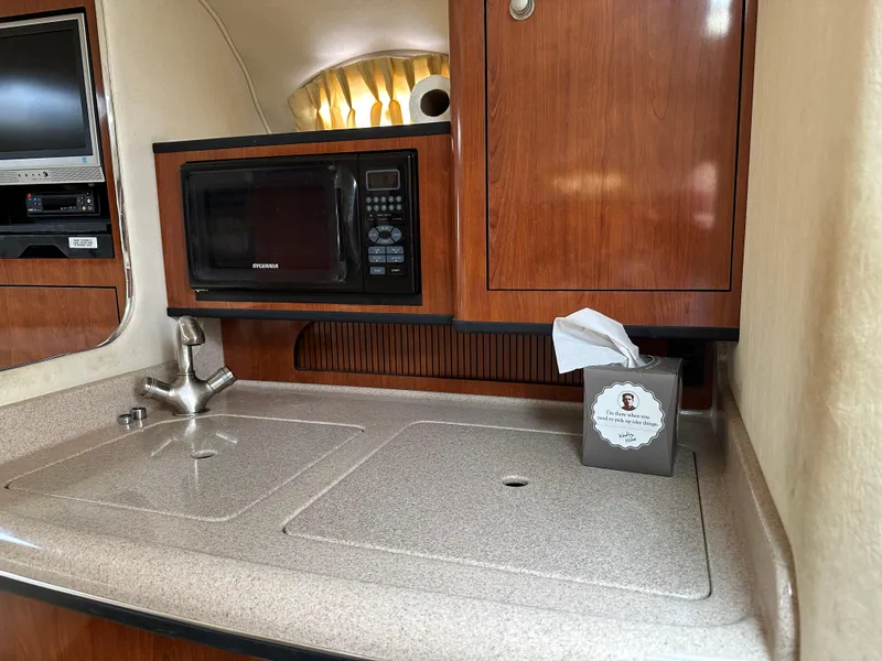 Slide: The Image of 2006 Sea Ray 280 Sundancer galley with microwave, sink, and wooden cabinetry. - 18