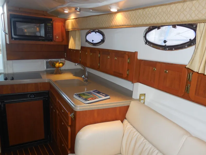 Slide: The Image of 2005 Stamas 370 Express yacht interior with kitchenette, featuring wood cabinets, microwave, and seating area. - 42