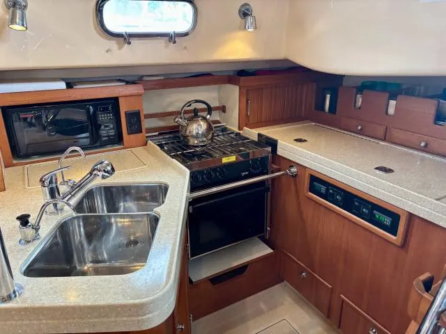 Slide: The Image of 2008 Island Packet 370 yacht kitchen with stove, sink, and microwave in wooden cabinetry. - 8