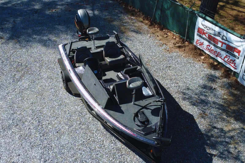 Slide: The Image of 2025 Skeeter ZX150 boat on gravel, near "Eat Sleep Fish" banner. - 2