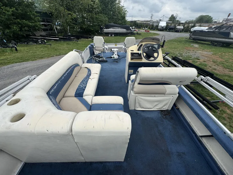 Slide: The Image of 2000 Starcraft 200 Classic pontoon boat with blue carpet and white seating, parked outdoors. - 16
