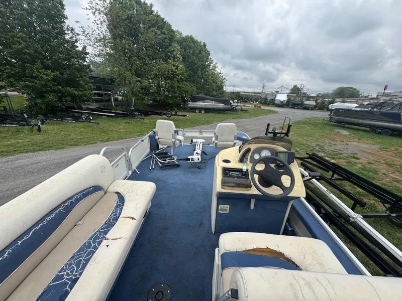 Slide: The Image of 2000 Starcraft 200 Classic pontoon boat with worn seating and steering console, parked outdoors. - 17