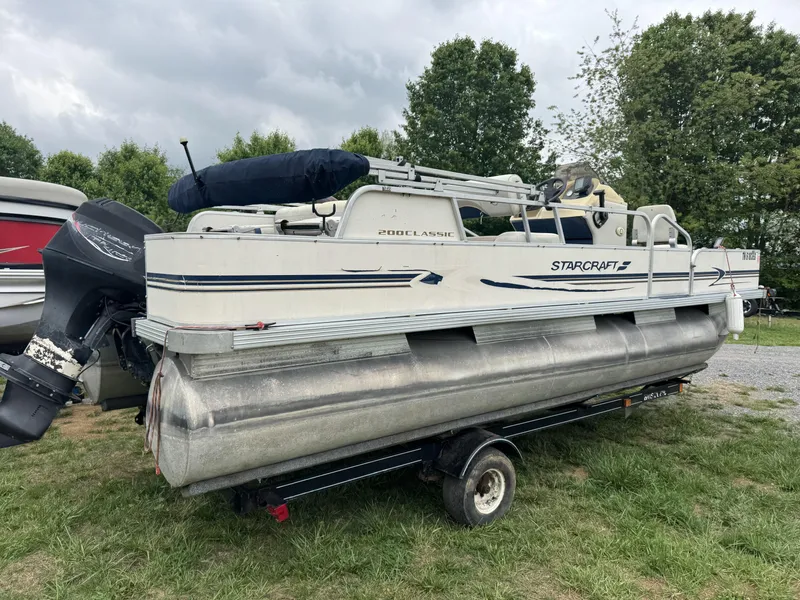 Slide: The Image of 2000 Starcraft 200 Classic pontoon boat on trailer, parked on grass with trees in background. - 4