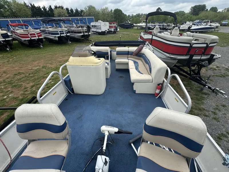 Slide: The Image of 2000 Starcraft 200 Classic pontoon boat with blue carpet and white seating, parked among other boats. - 6