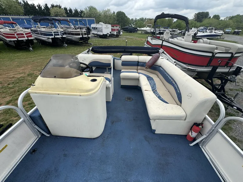 Slide: The Image of 2000 Starcraft 200 Classic pontoon boat with blue carpet and white seating, parked among other boats. - 7