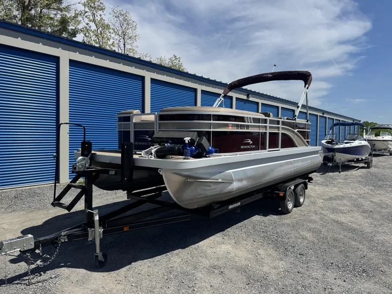 Slide: The Image of 2022 Bennington 22 SXSR pontoon boat on trailer near blue storage units. - 14