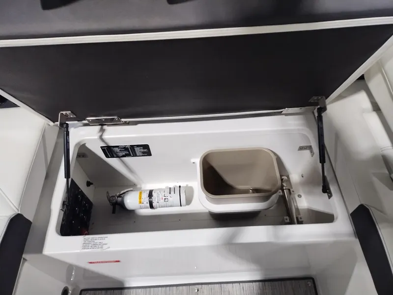 Slide: The Image of Storage compartment in a 2025 Cobalt R6 Surf boat, featuring a fire extinguisher and bin. - 23