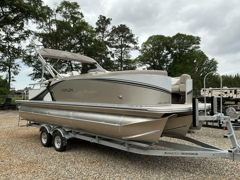 Slide: The Image of 2025 Avalon LSZ 23 Rear Lounger pontoon boat on trailer, parked outdoors. - 1