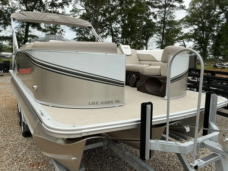 Slide: The Image of 2025 Avalon LSZ 23 Rear Lounger pontoon boat on trailer, beige and white design. - 2