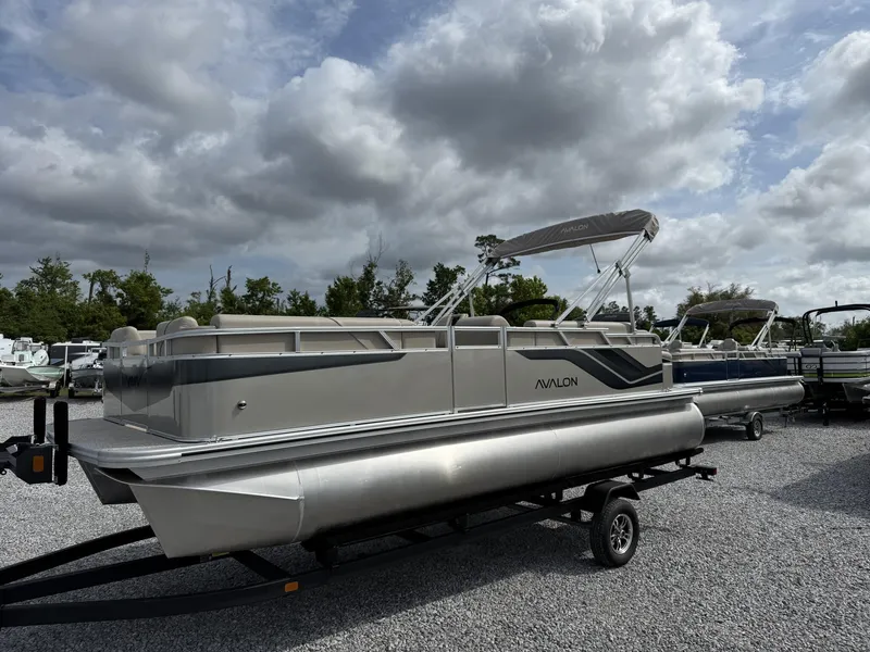 Slide: The Image of 2025 Avalon Venture 21 CRUISE pontoon boat on trailer, parked outdoors under cloudy sky. - 1