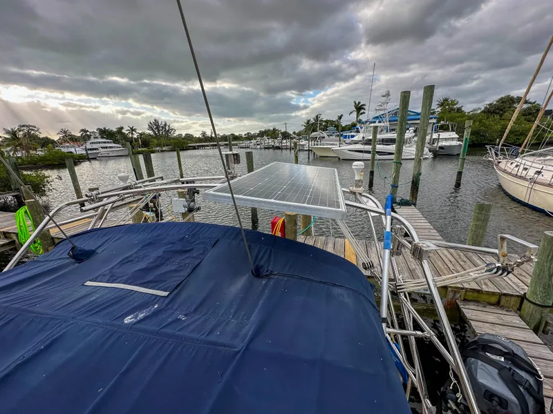 Slide: The Image of 2005 Island Packet 370 sailboat docked, featuring solar panels and a blue canopy under cloudy skies. - 8