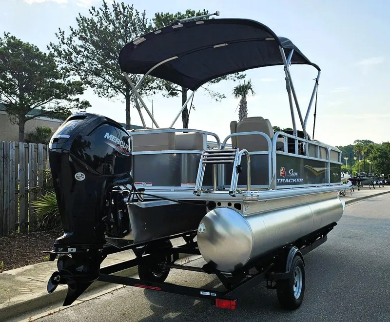 Slide: The Image of 2025 Sun Tracker Party Barge 18 DLX pontoon boat on trailer, with canopy and Mercury engine. - 2