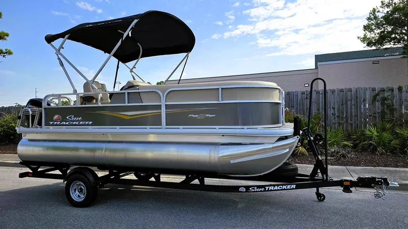 Slide: The Image of 2025 Sun Tracker Party Barge 18 DLX pontoon boat on trailer, parked outdoors. - 4