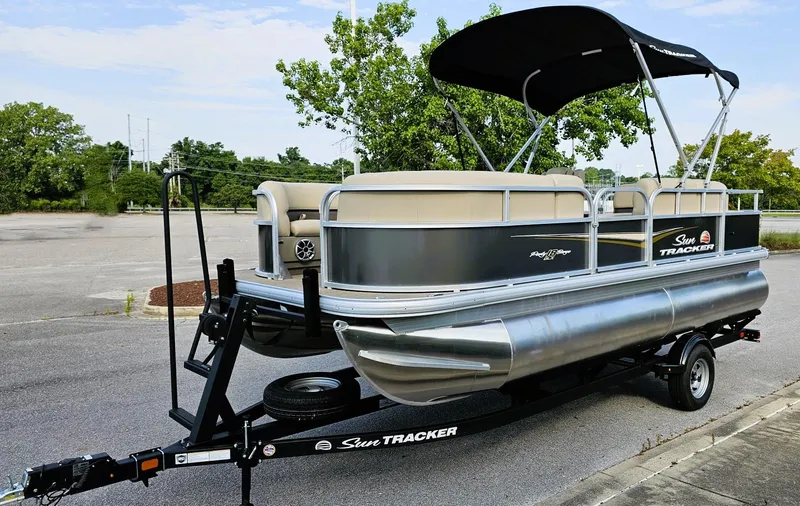 Slide: The Image of 2025 Sun Tracker Party Barge 18 DLX pontoon boat on trailer, parked outdoors. - 6