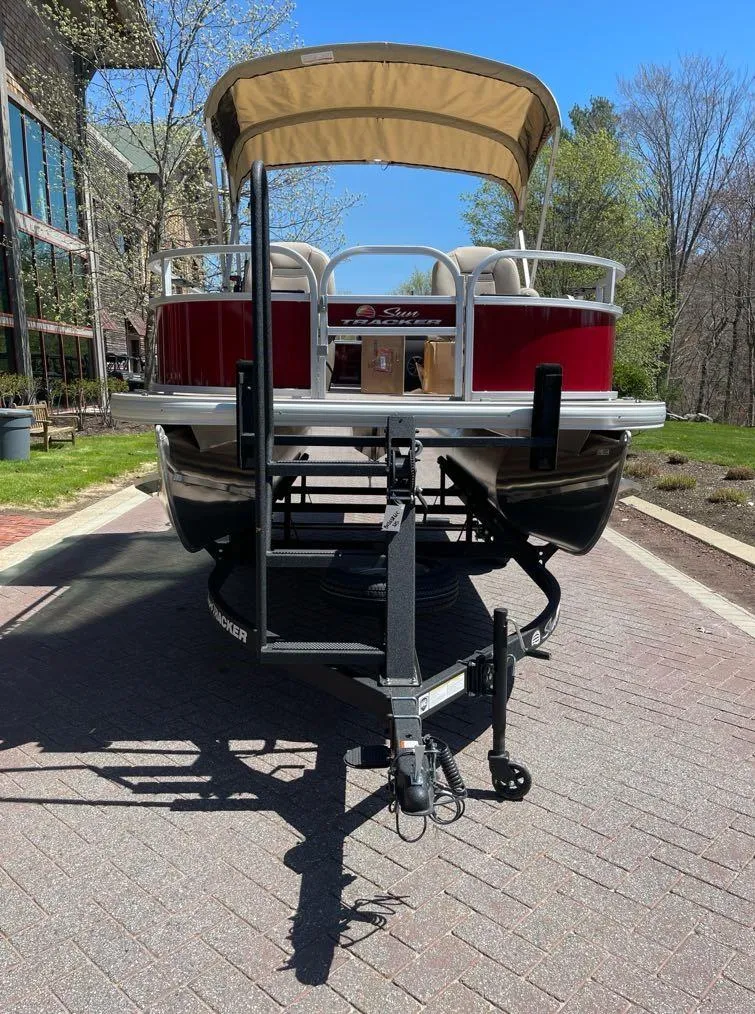 Slide: The Image of 2025 Sun Tracker Bass Buggy 16 XL Select pontoon boat on trailer, parked outdoors. - 2