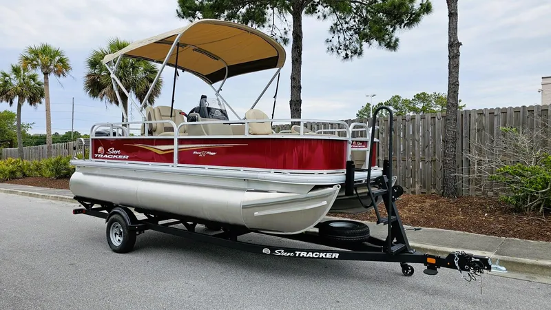 Slide: The Image of 2025 Sun Tracker Bass Buggy 18 DLX pontoon boat on trailer, parked outdoors. - 2