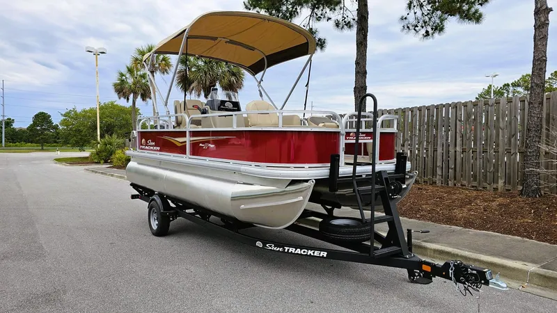 Slide: The Image of 2025 Sun Tracker Bass Buggy 18 DLX pontoon boat on trailer, parked outdoors. - 6