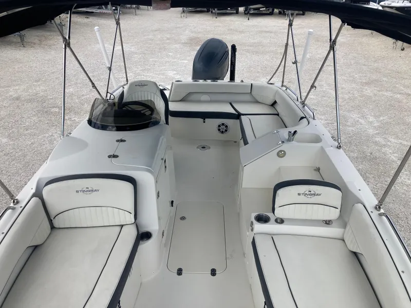 Slide: The Image of 2020 Stingray 212 boat interior with seating and steering console, parked on gravel. - 12