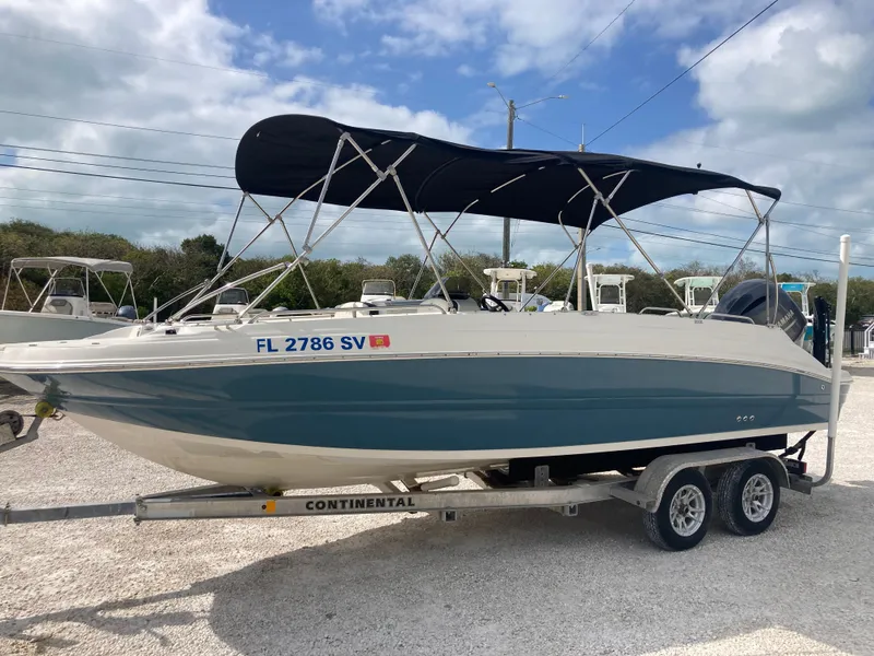 Slide: The Image of 2020 Stingray 212 boat on trailer with canopy, parked outdoors under cloudy sky. - 5