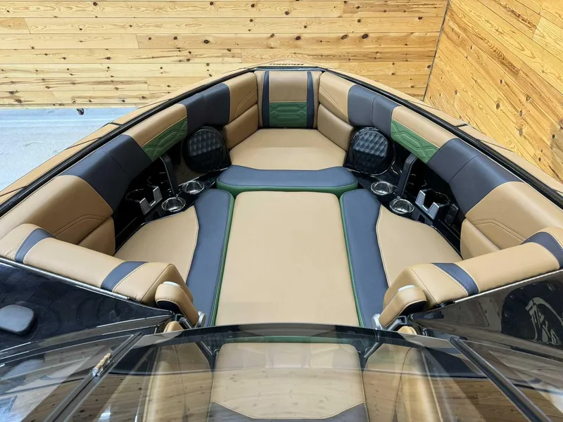 Slide: The Image of 2023 Malibu 25 LSV boat interior with tan and black seating, wooden backdrop. - 7