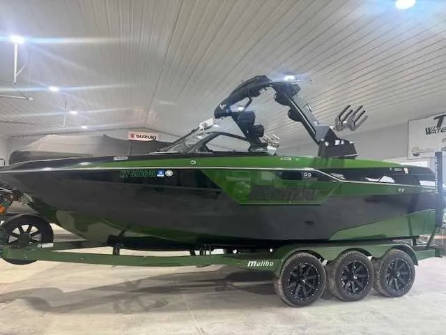 The Image of 2022 Malibu M240 boat in showroom, green and black design on trailer. - 1