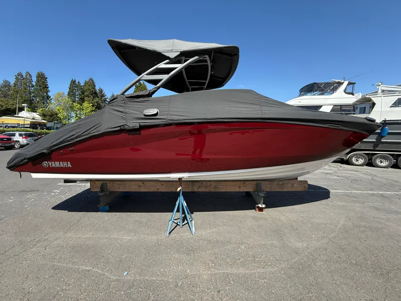 Slide: The Image of 2022 Yamaha Boats 252SD, red hull, covered, parked outdoors on a sunny day. - 2