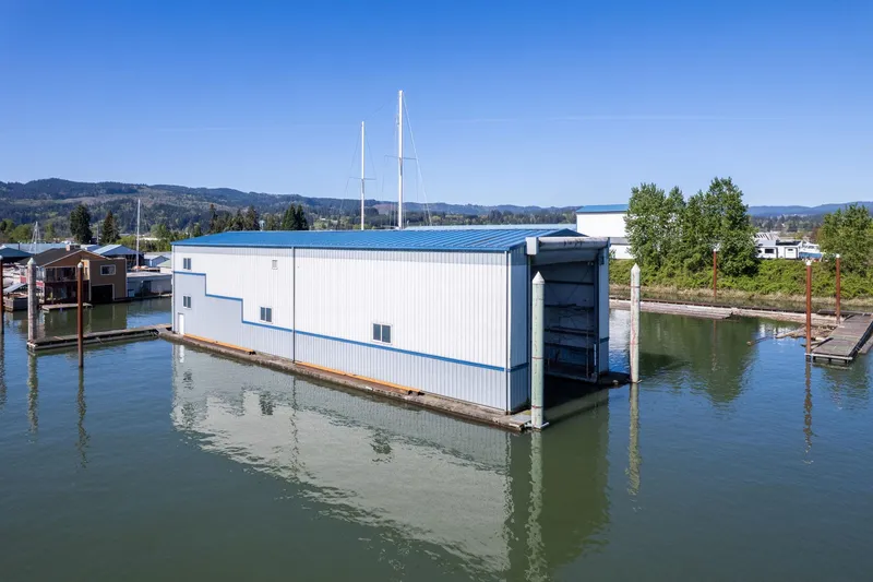 The Image of Floating boathouse on calm water, Custom Larson model, 1985, with blue roof and scenic backdrop. - 0