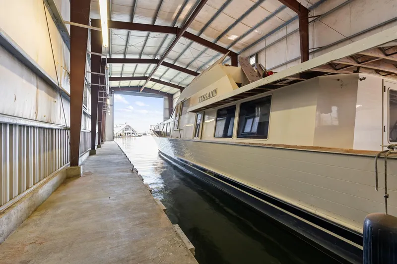 Slide: The Image of 1985 Custom Larson Boathouse with boat docked inside, featuring metal roof and concrete walkway. - 13