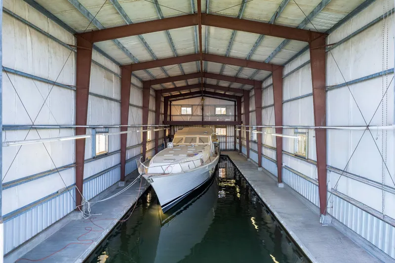 Slide: The Image of A 1985 Custom Larson Boathouse with a yacht docked inside, featuring metal beams and waterway. - 16