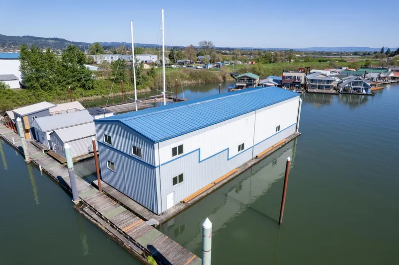 Slide: The Image of Aerial view of 1985 Custom Larson Boathouse on calm water, blue roof, surrounded by docks. - 2