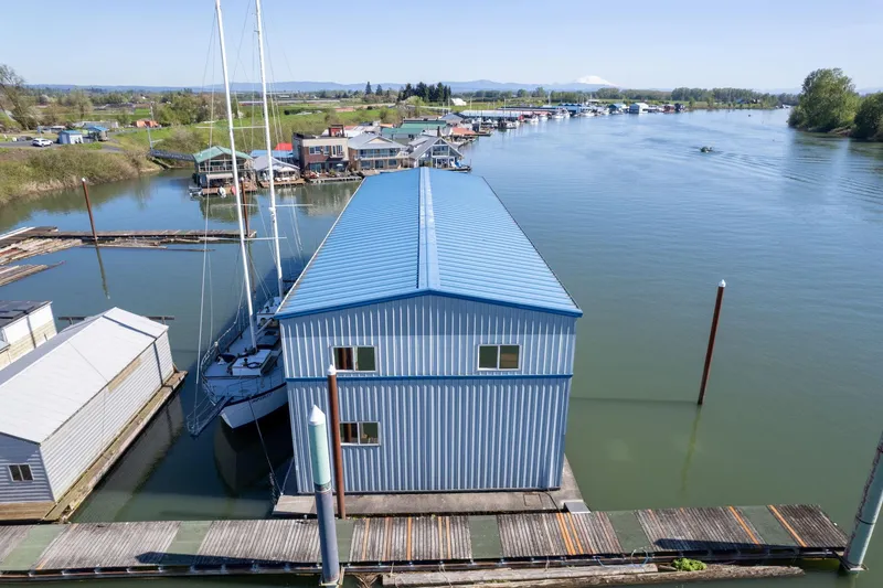 Slide: The Image of Blue boathouse on calm river, surrounded by docks and trees, under clear sky. - 20