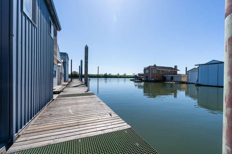 Slide: The Image of Wooden dock beside calm water at Larson Boathouse, 1985 model, under clear blue sky. - 31