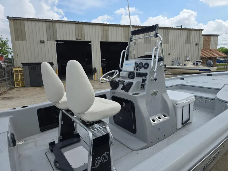 Slide: The Image of 2016 Blue Wave 2400 PureBay boat with dual seats and control panel, parked near a warehouse. - 9