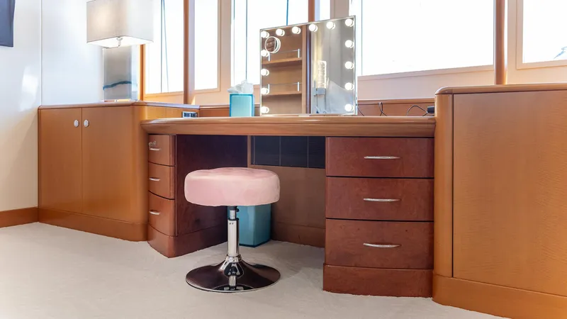 Slide: The Image of Vanity area with wooden desk, pink stool, and illuminated mirror on Feadship TASIA yacht. - 12