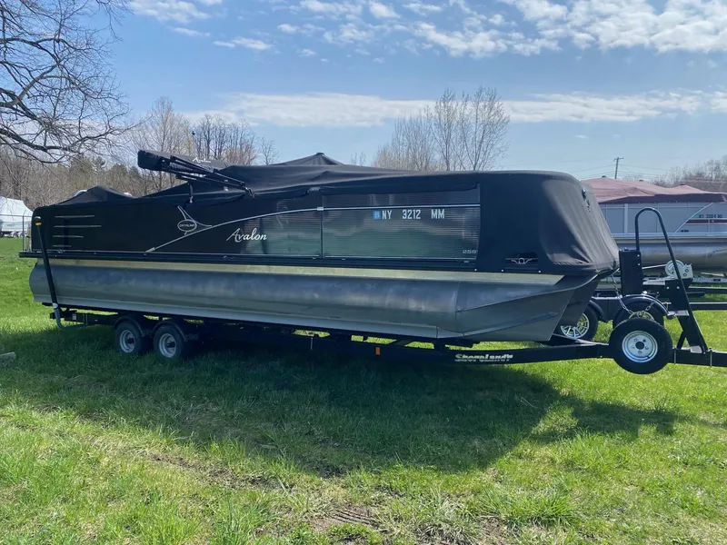 Slide: The Image of 2017 Avalon 2585 RF pontoon boat covered on a trailer, parked on grass. - 0