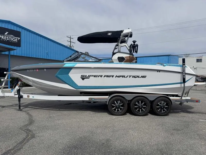 Slide: The Image of 2019 Nautique G25 boat on trailer, blue and white design, parked outside Prestige building. - 1