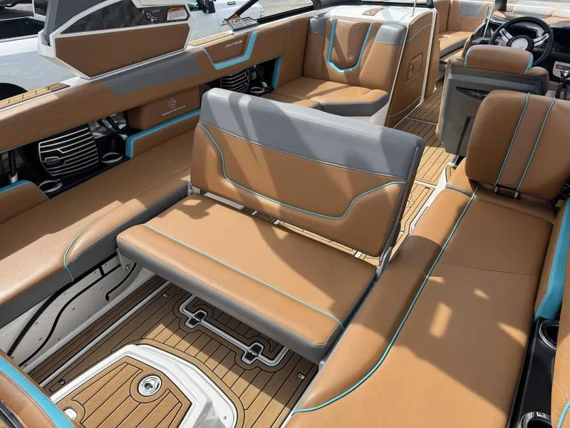 Slide: The Image of 2019 Nautique G25 boat interior with tan and gray seating, featuring blue accents and teak flooring. - 2