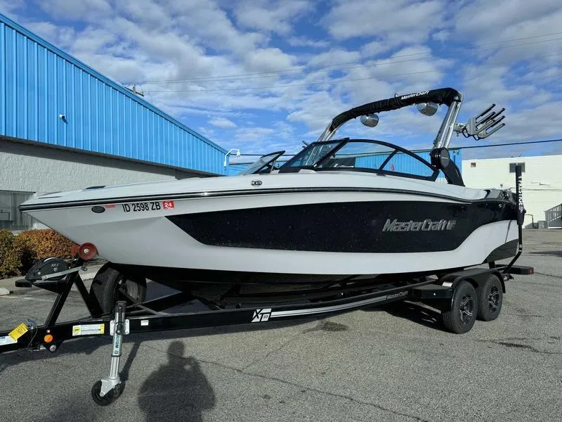 Slide: The Image of 2022 MasterCraft XT23 boat on trailer, parked outdoors near blue building. - 2